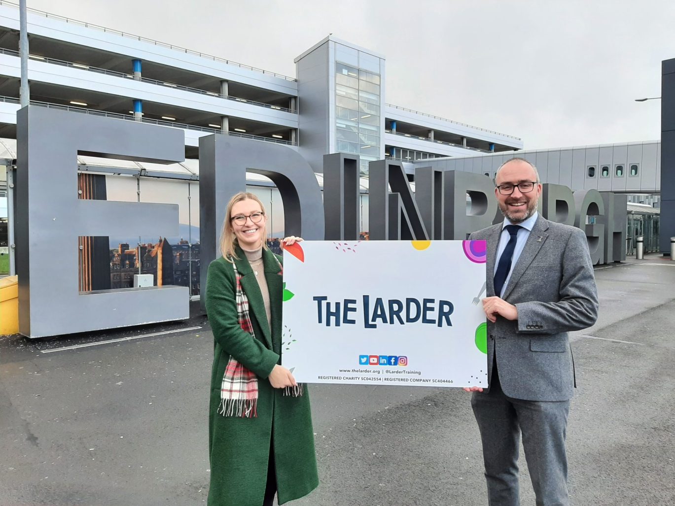 Woman and man holding sign saying The Larder