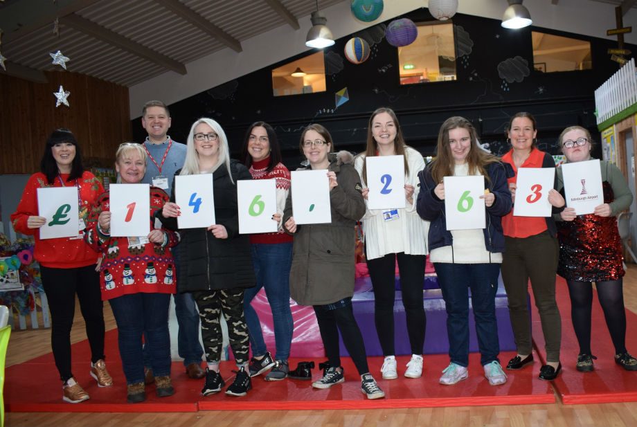 A line of people smiling and holding up numbers to show a total of £146,263