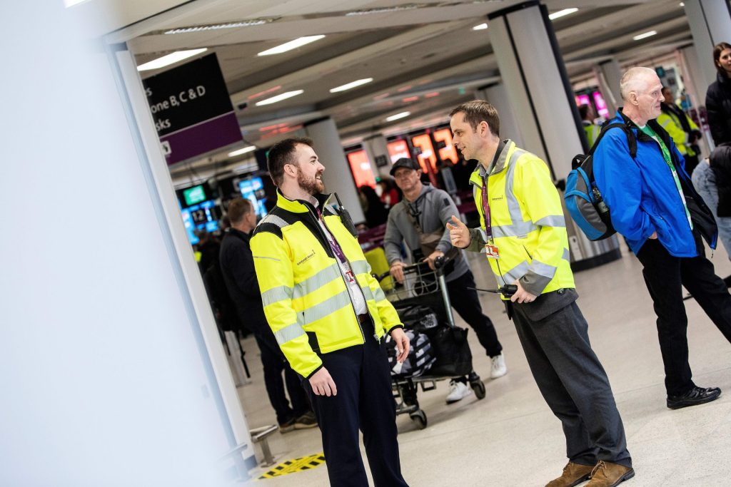 Two colleagues in high vis vests, chatting in a busy terminal